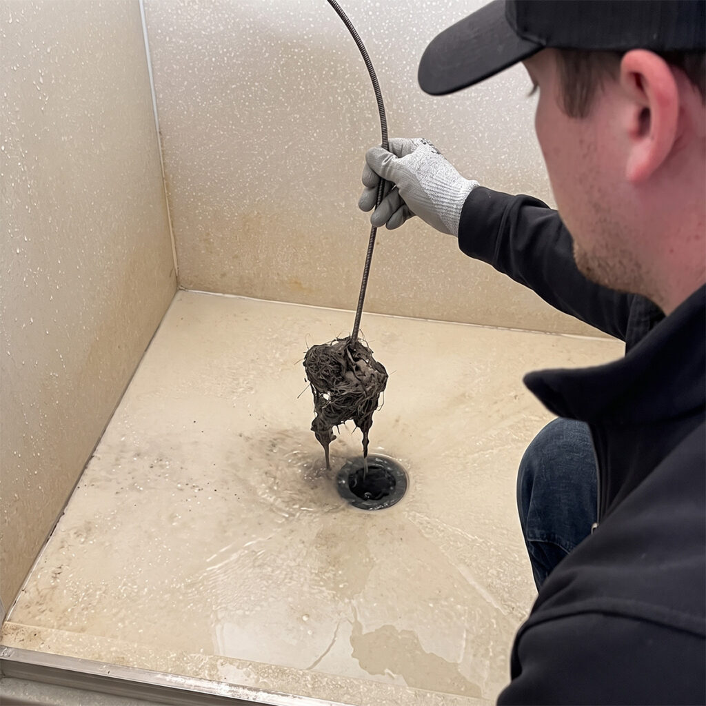 Plumber pulling clogged hair and debris from shower drain with snake tool