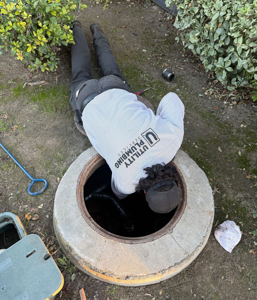 Utility Plumbing Services technician reaching into open sewer cleanout access