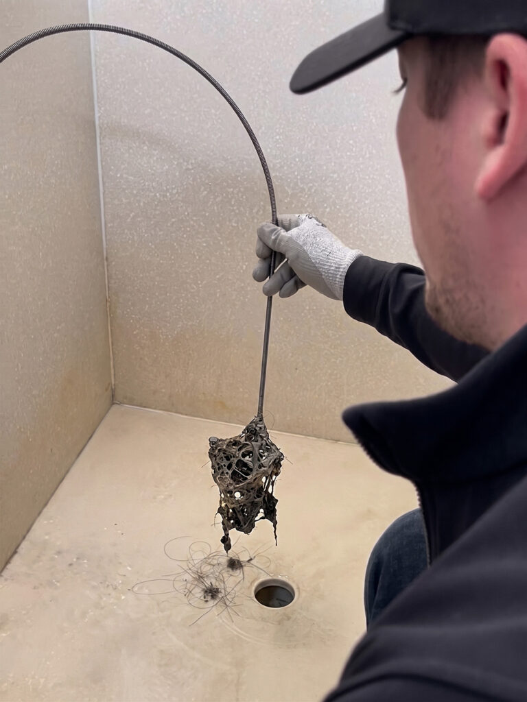 Cody pulling large hair clog from shower drain with snake tool