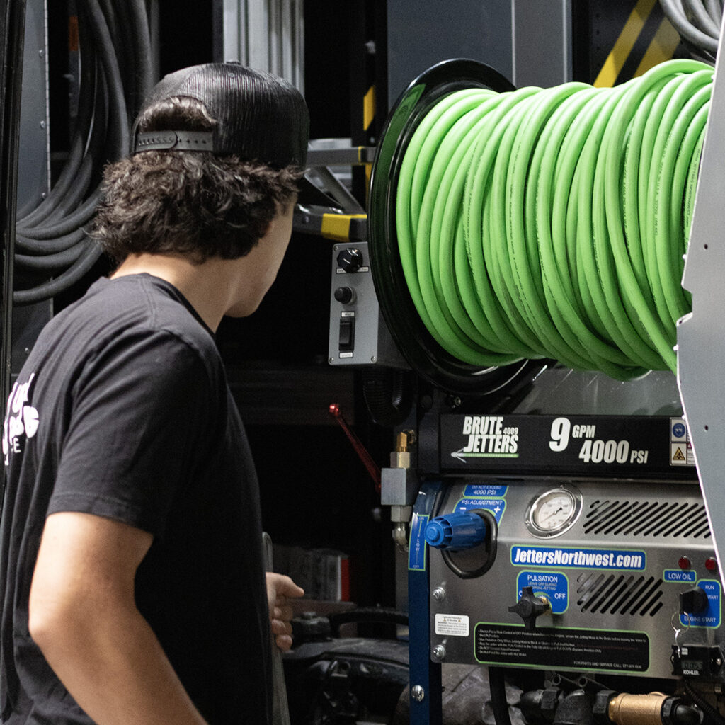 Plumber operating hydro jetter machine with green hose for drain cleaning